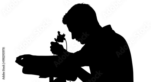 Silhouette of a tattoo artist working on a client's arm with a tattoo machine