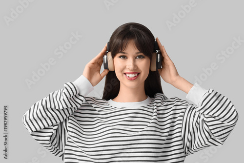 Smiling young woman in headphones on light background