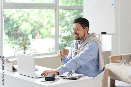 Young male teacher with laptop and cup of coffee giving online lesson at home