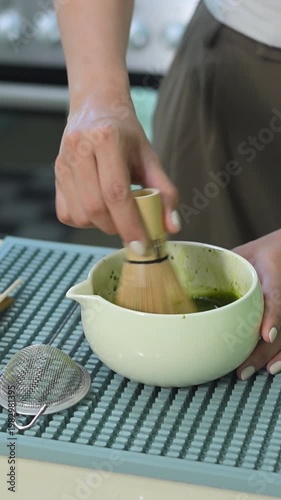 Close up of woman whisking matcha tea with bamboo chasen in kitchen.