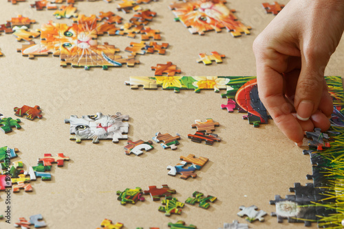 A woman is assembling puzzles at home in natural light. Only hands are visible.