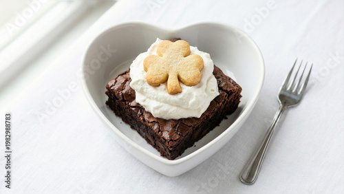 gourmet chocolate brownie with whipped cream and clover shaped smiley cookie in a heart shaped bowl isolated on white background