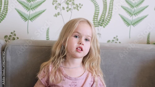 Child girl at home on the couch attentively watching TV with her mouth open