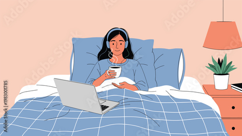 Young woman wearing headphones sits comfortably in her bed working on a laptop while holding a steaming mug of coffee.
