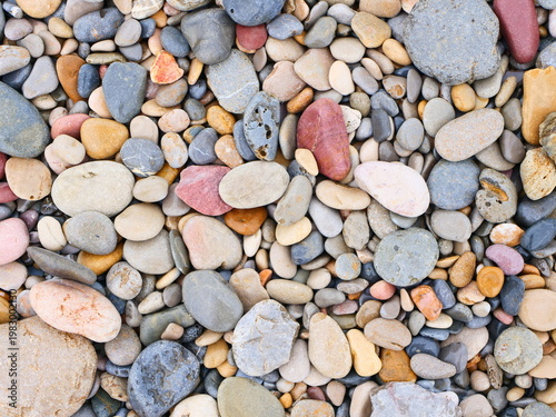 Different kinds of stones and pebbles are found on the ground. The stones show multiple colors and sizes, forming a natural pattern. This scene is common in outdoor areas like beaches or riverbanks