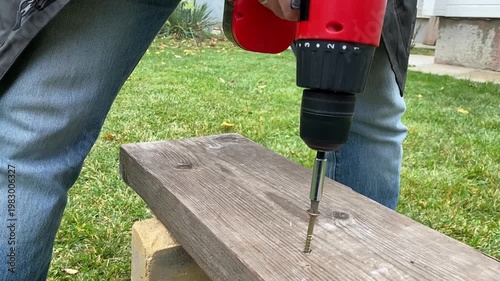 close up of cordless screwdriver pulling screw out of wooden board reverse rotation diy repair and disassembly process power tool in action workshop detail shot