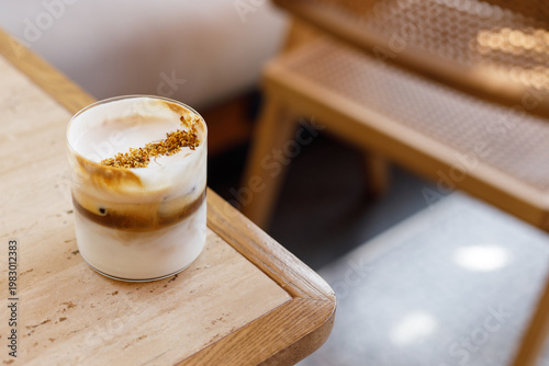 Cup of creation coffee drink and milk foam decorated with Osmanthus flower on wooden table by the window.