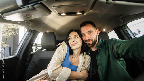 Young couple taking a selfie inside a car, smiling and enjoying their time together, with the car's interior and cityscape visible through the windows