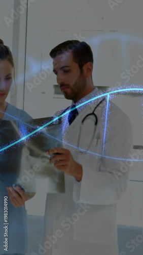 Vertical video: Doctor pointing at X-ray causing blue helix while nurse holding film reviewing scan