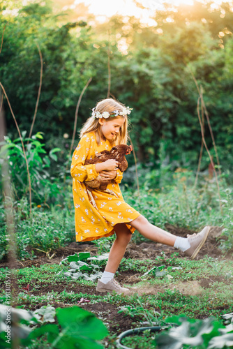 Girl holds a chicken while playing in a garden at sunset