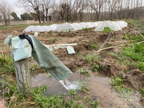 Irrigation system waters a muddy field with green tarp and plastic tunnels in background