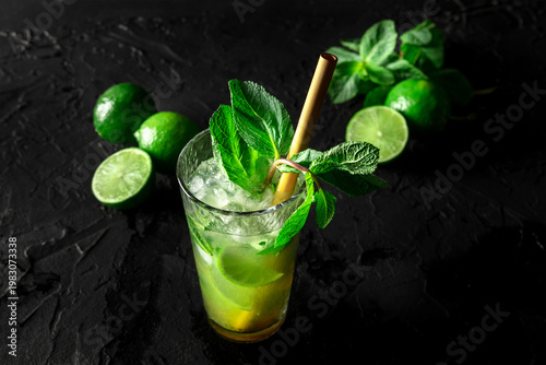 Mojito, summer cocktail with mint and ice, a single glass on black with limes