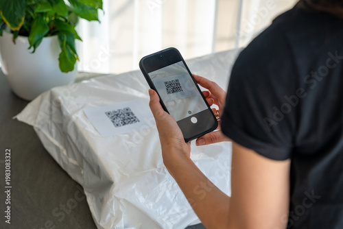 Fotografia Person scanning QR code on parcel with smartphone camera for delivery tracking at home