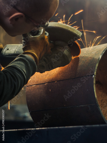 Industrial metalworker using angle grinder on steel with bright sparks. Back view of manual labor in workshop. Metal fabrication, engineering, and professional craftsmanship concept. Action close-up.