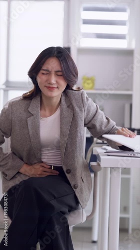 Asian adult woman experiencing severe stomach pain at office desk unable work closing laptop due to illness or stress