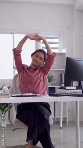 Asian adult woman professional worker stretching arms overhead relaxing at bright modern home office desk improving posture combating fatigue during remote work