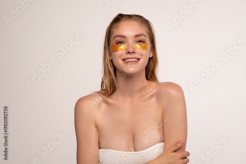 Woman with gold eye patches smiling, engaging with skin care, enjoying beauty treatment and wellness routine at spa