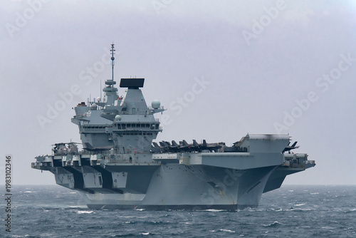 Royal Navy aircraft carrier HMS Prince of Wales sailing in Tokyo Bay, Japan, with F-35B fighter jets on deck, rough and cloudy weather.