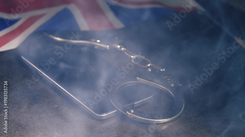 Mobile phone evidence and police handcuffs and British flag with smoke on desk