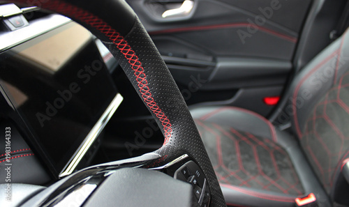 Red stitching on a steering wheel against a defocused car interior with red stitched leather upholstery
