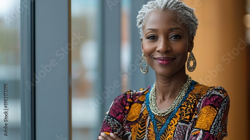 Confident woman with short gray hair, wearing colorful patterned dress and jewelry, smiles warmly at the camera