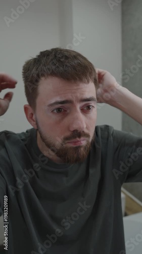 White man inspecting facial skin in bathroom mirror, checking irritation and beard texture, gentle touching of cheek, soft morning