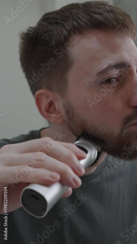 White man edging sideburns and cheekline with electric trimmer, side profile closeup, steady hand guiding clipper, neutral