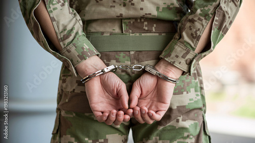 A person in military camouflage uniform with hands cuffed behind their back, facing away from the camera.