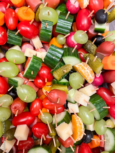 Top view of assorted canapes with vegetables, fruits, cheese and sausages on wooden skewers, party food and appetizer