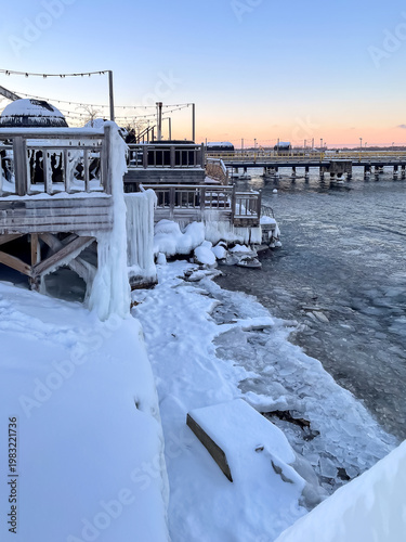 Wooden embankment completely covered with thick ice in winter day, ice chunks floating in sea, cold weather and seasonal nature