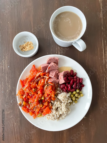 Top view of plate with balanced meal of pearl barley, pate, red beans, stewed vegetables, small cookie and coffee with milk, healthy eating and nutrition