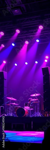 Center stage drum kit bathed in pink and blue light, flanked by towering speaker stacks on elevated platform,  speakers,  expression