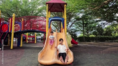 Two happy little Indonesian girls playing together in an outdoor playground. Slow motion.