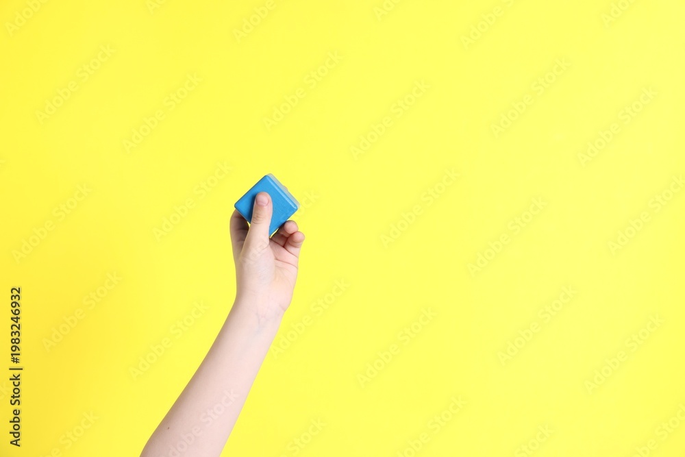 Fototapeta premium Child with blue cube on yellow background, closeup. Space for text