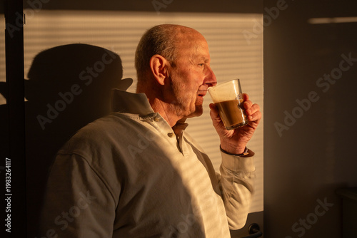 Stockholm, Sweden A man drinks coffee in the early morning in the shadow of window shades.