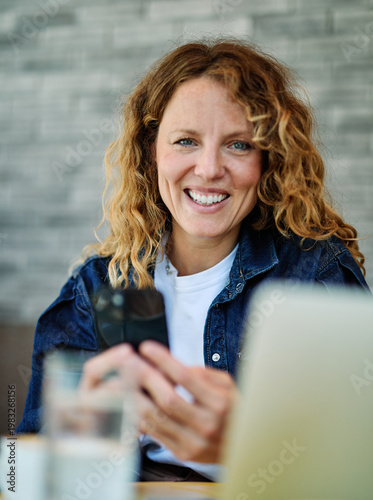 Portrait of a smiling young woman girl using a mobile phone and laptop computer with a coffee cup in a coffee shop or a restaurant in the city, tourists visiting destination, or entrepreneur businessm