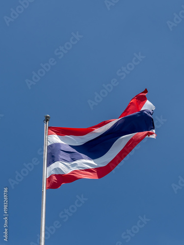 The flag of Thailand waving in the wind with blue sky in the background. Thailand is a Southeast Asian country.