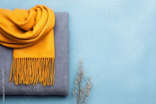 Cozy yellow scarf draped over a soft gray blanket on a textured blue background