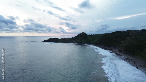 Aerial view of tropical coastline with waves and hills at sunset