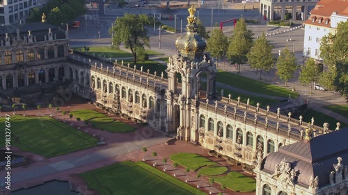 Aerial view of the Dresden Zwinger at sunset. The Crown Gate and galleries cast long shadows over the manicured courtyard with its lush green lawns and Baroque architecture.