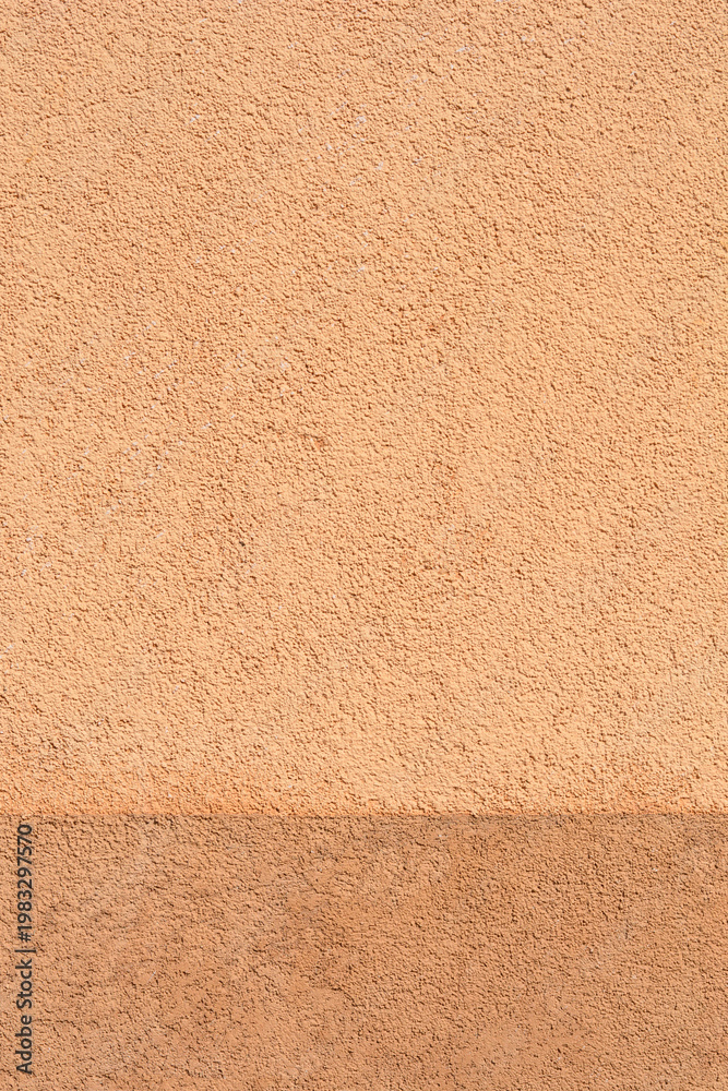 Fototapeta premium Horizontal division between light and dark pastel apricot stucco wall texture with a rough sandy finish suitable for architectural backgrounds.