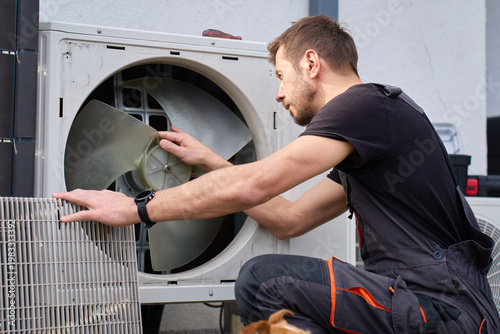 Technician removing front cover and inspecting fan inside outdoor heat pump unit. Concept of HVAC maintenance repair service and energy efficient home heating and cooling
