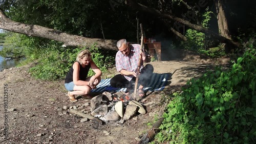 A man and a woman are preparing a barbecue on an open fire near the river.