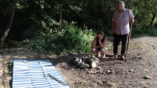 A man and a woman are preparing a barbecue on an open fire near the river.