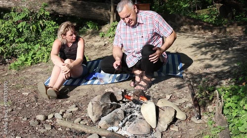 A man and a woman are preparing a barbecue on an open fire near the river.