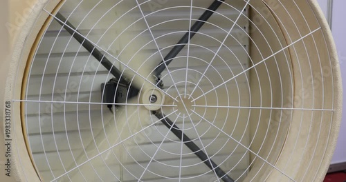 Close up of industrial ventilation fan rotating behind protective metal grid in factory interior. Air circulation system with safety design used in manufacturing and industry environment.