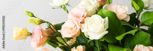 Fresh roses and eustomas are arranged in a bouquet with green leaves. The setting has a plain background and bright lighting. This moment captures floral beauty, banner