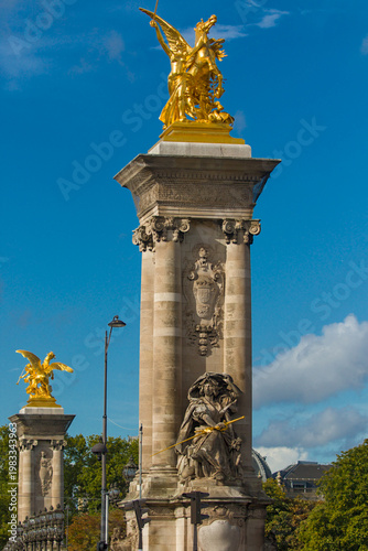 Golden Pegasus crowns a column on Pont Alexandre III. Carved figures and crests decorate the base. A second gilded statue behind echoes the ornate style.