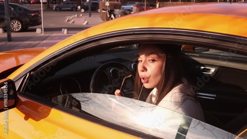 Stylish young woman putting on sunglasses and closing car window in yellow car on parking lot. Perfect for automotive, lifestyle, fashion and urban travel themed commercial projects