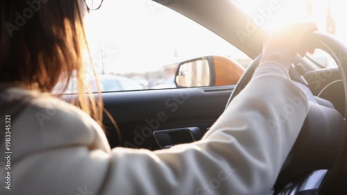Back view of young woman driving car in bright sunlight with lens flare. Perfect for travel, road trip, freedom, lifestyle and transportation themed commercial projects
